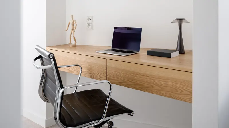 Minimalist wooden desk with a single laptop and lamp.